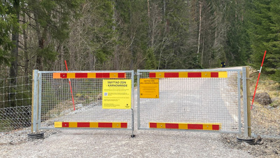 Stängsel med förbudsskyltar vid väg i skogsområde.