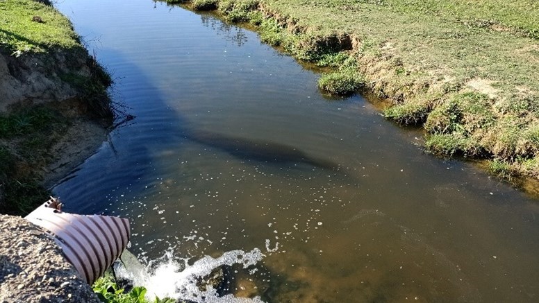 Vatten rinner ur ett avloppsrör i en å