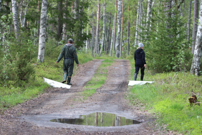 Två personer går längs en skogsväg och drar varsitt vitt tygstycke bakom sig.