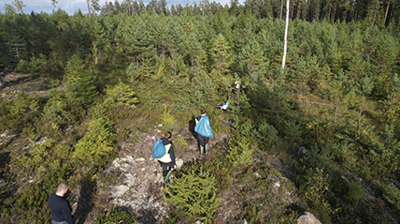 Människor med blå soppåsar vandrar över berg mot skog.