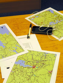 Tre papperskartor, en penna och en mobiltelefon med headset litgger på ett träbord. 